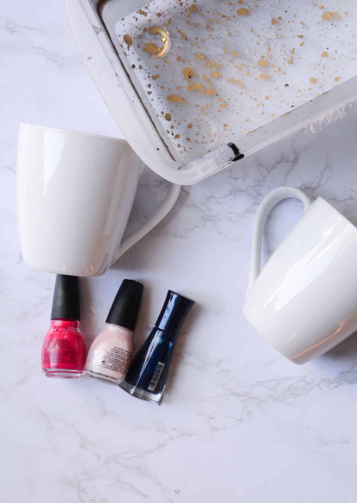 2 white ceramic mugs, nail polish and plastic container filled with water.