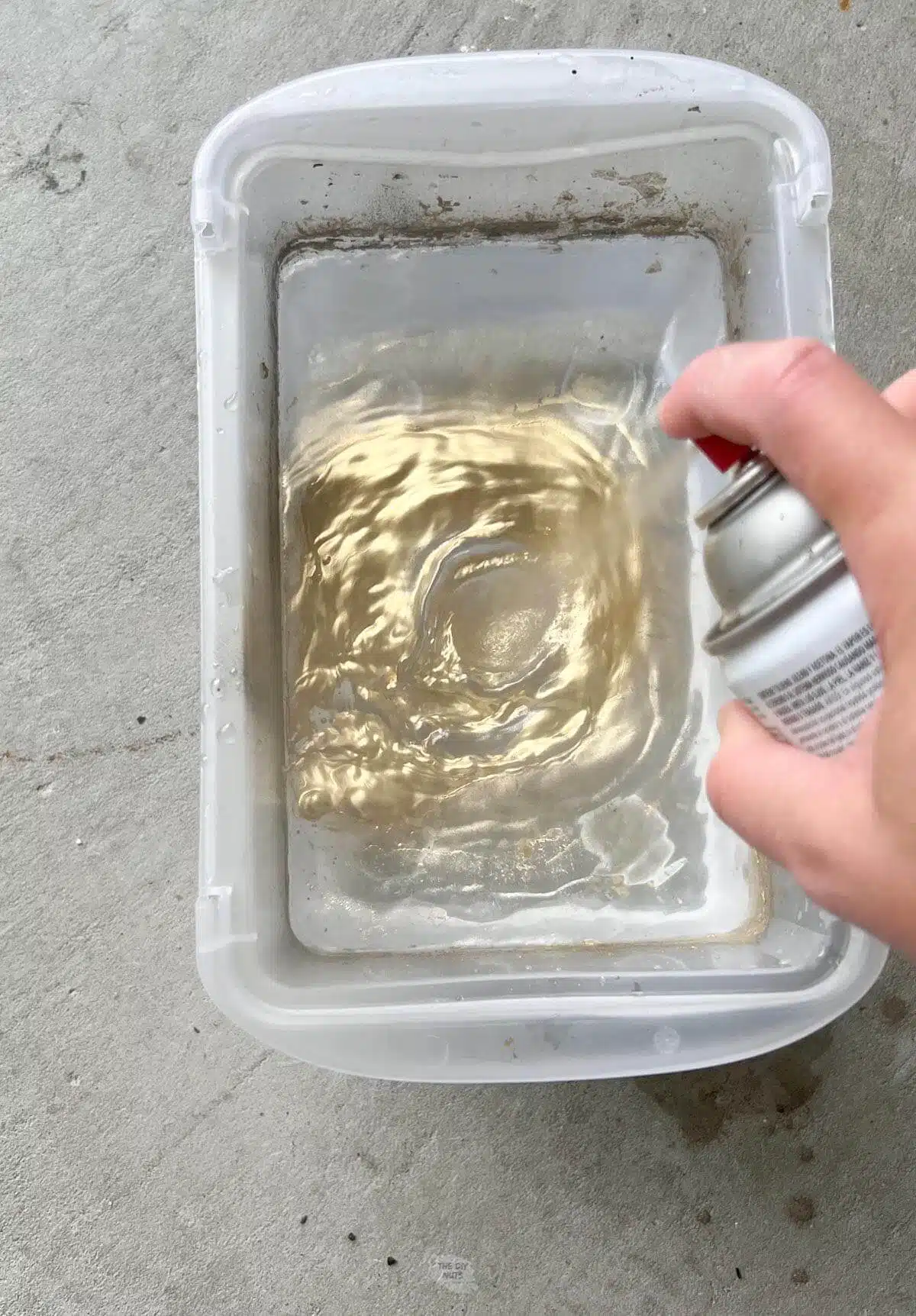 hand spraying gold spray paint into plastic container with water.