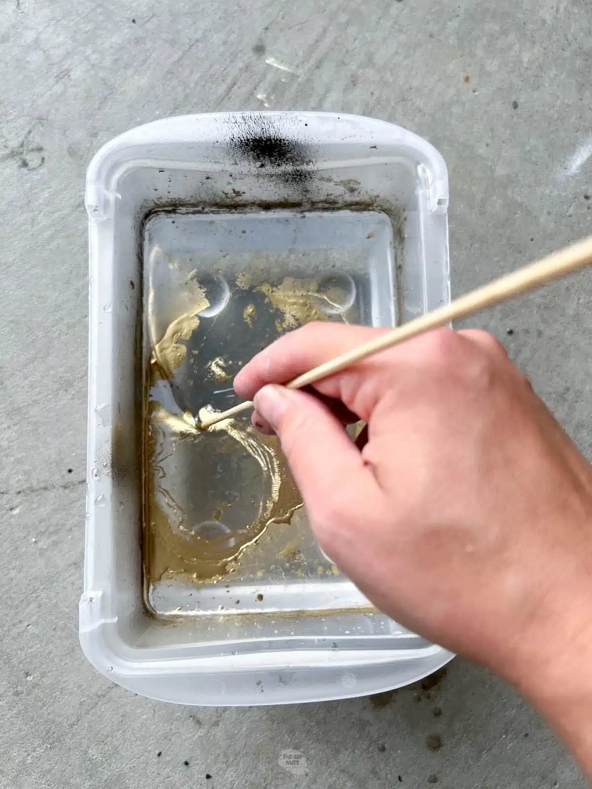 hand using skewer to swirl spray paint around in water.
