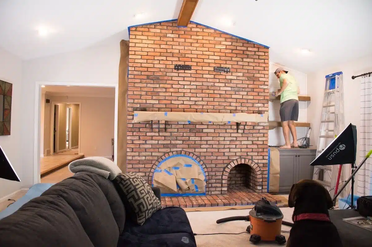 man standing on cabinets by brick fireplace adding painter's tape and paper.