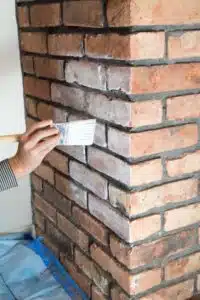 hand holding paint brush painting a brick fireplace.