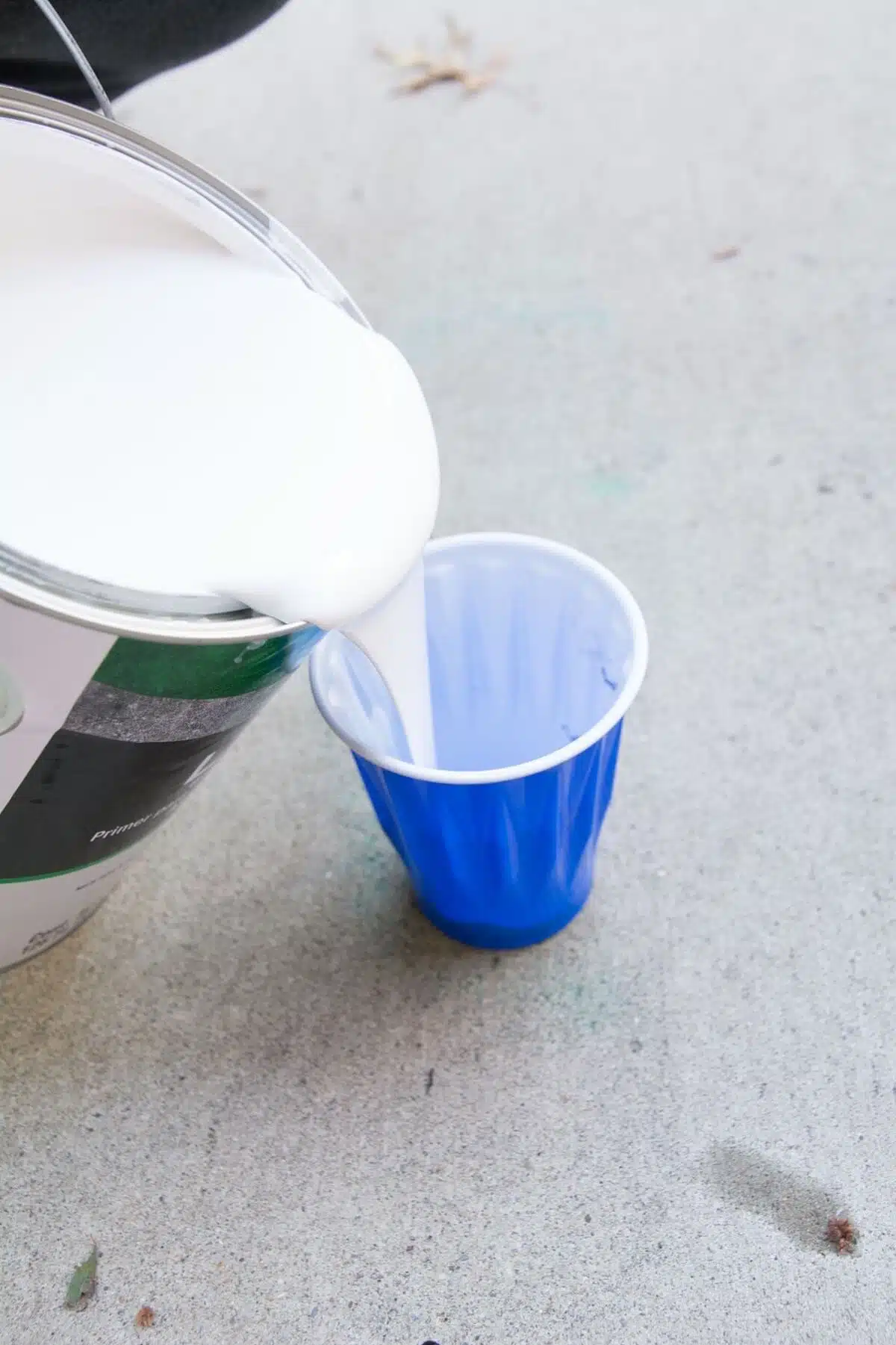 pouring white masonry paint into small blue cup.