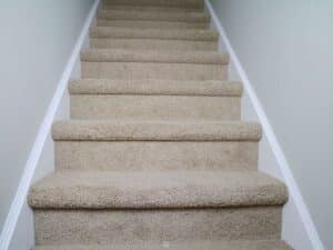 beige carpet on stairs with white molding and neutral walls.