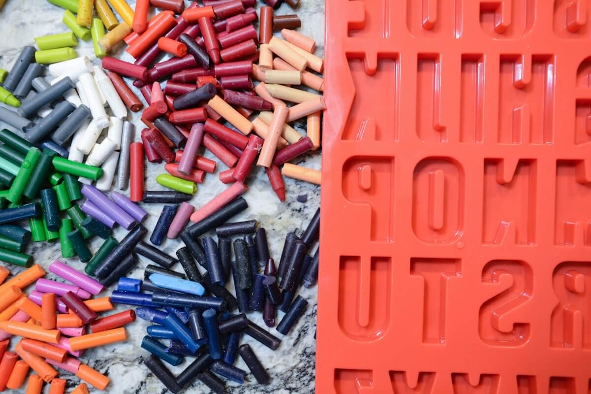pile of different crayons on counter next to red silicone letter mold.