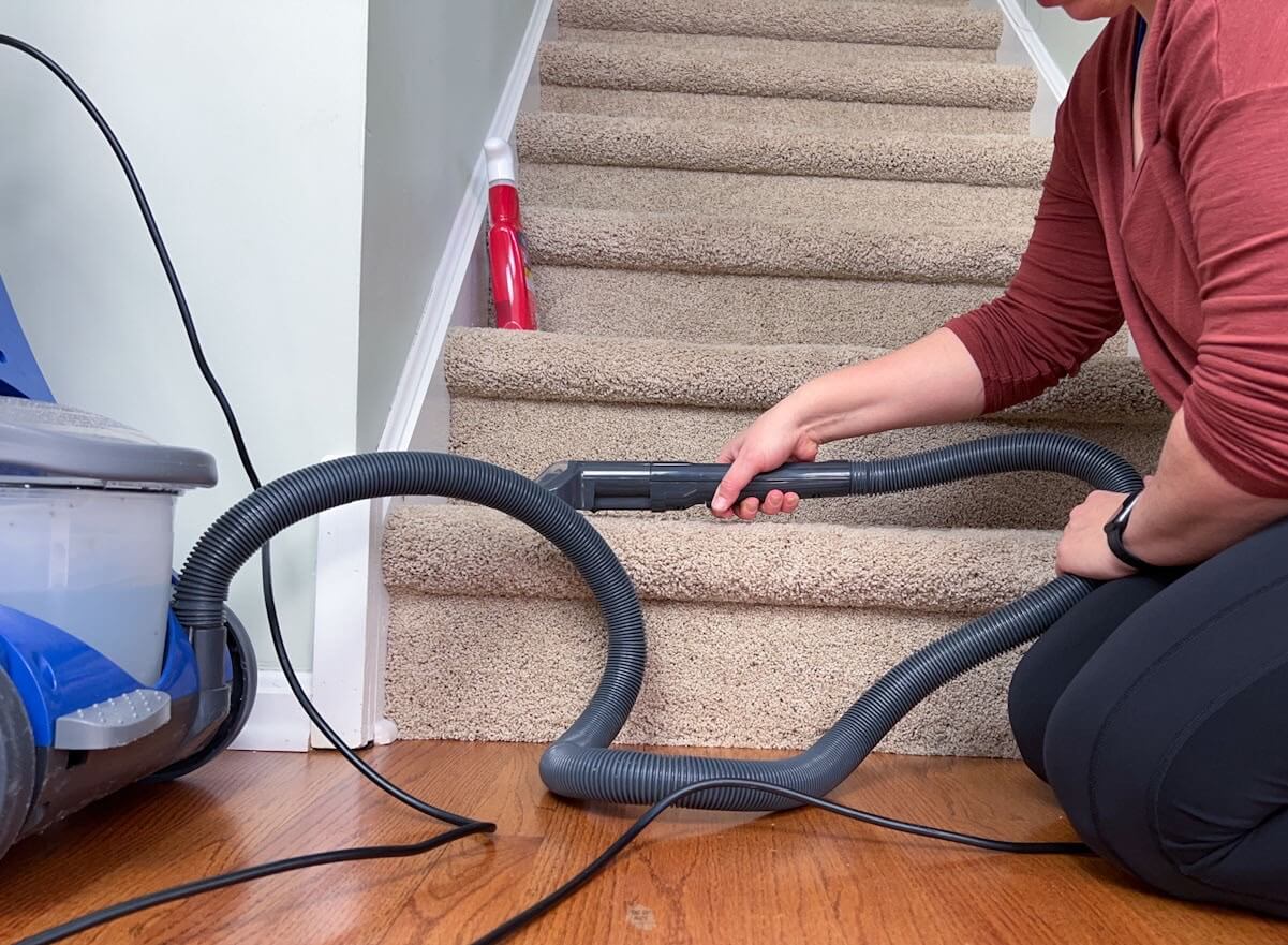 woman using Bissel carpet cleaner on carpeted steps.