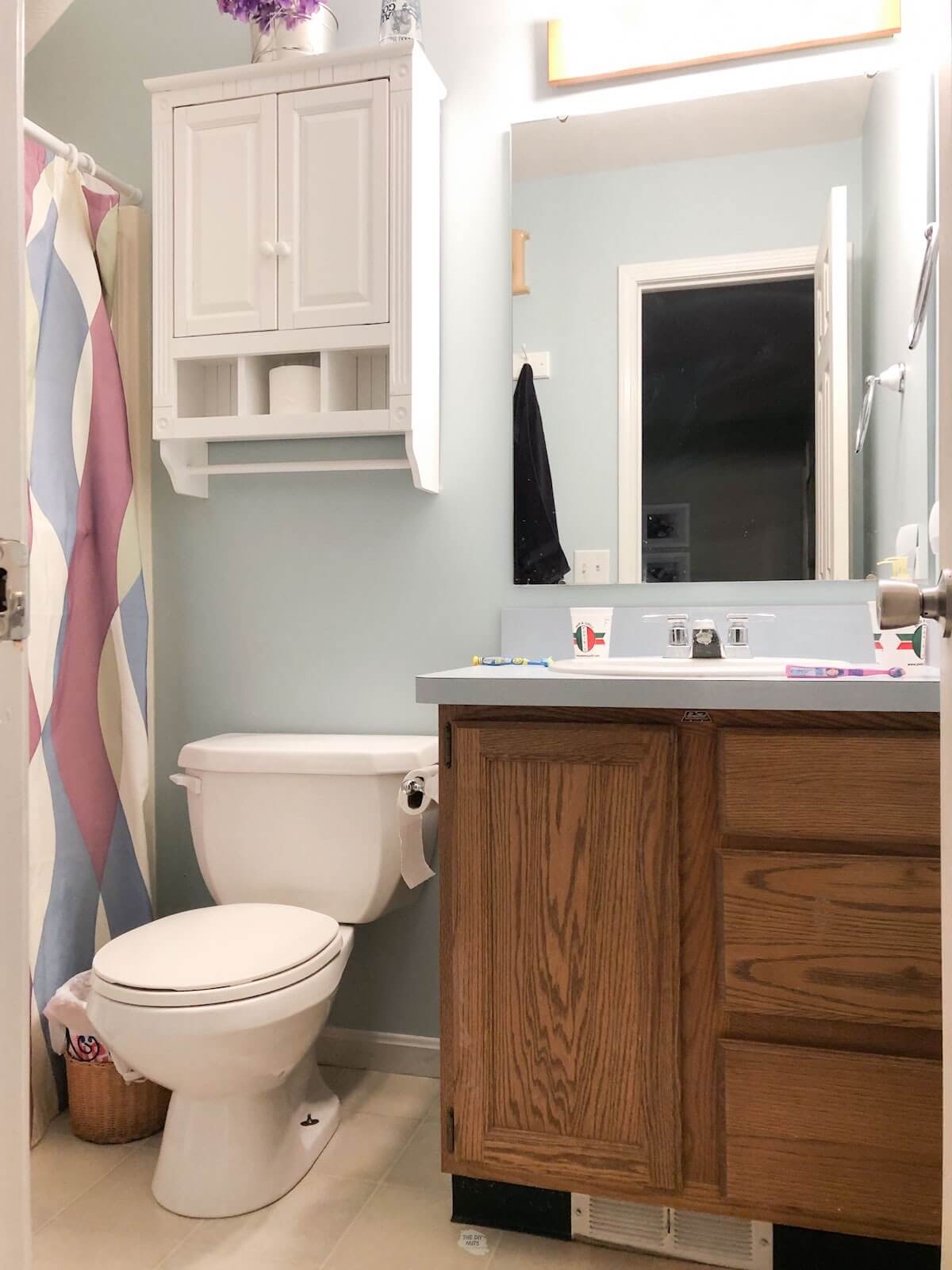 Dated oak cabinet vanity in small bathroom with blue walls, toilet and white cabinet on wall.