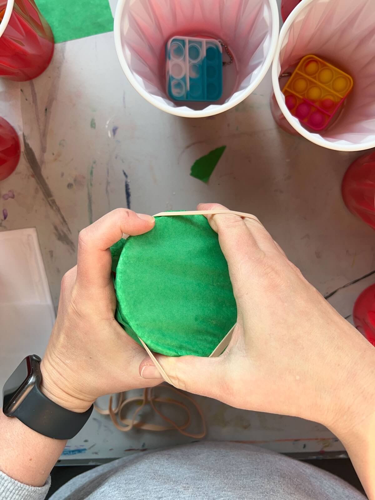 hands putting green tissue paper on cup with rubber band.