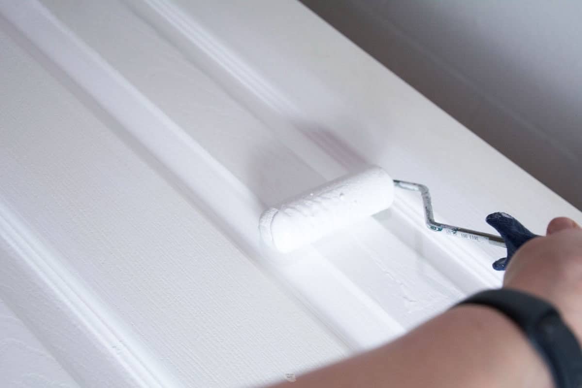 hand using roller to paint door white.