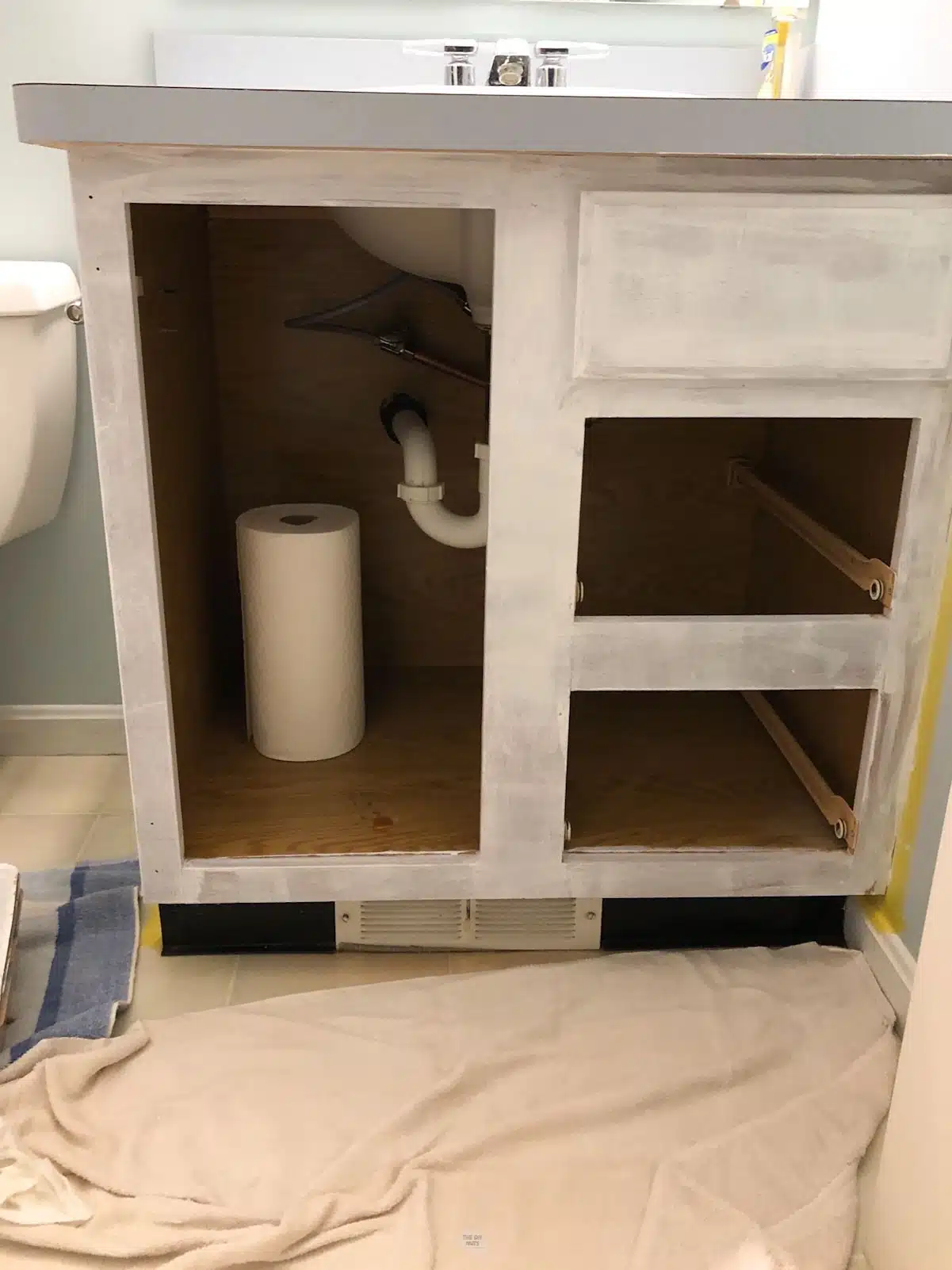 white primer on bathroom vanity cabinet box with drop cloth on the floor.