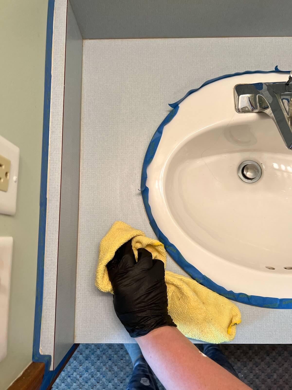 hand wearing black glove using yellow rag to wipe down bathroom countertops.