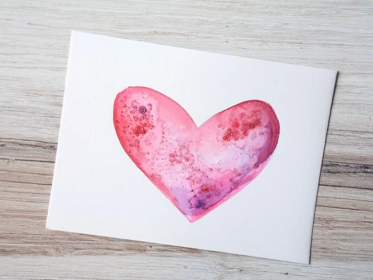 red & purple watercolor heart painted on white paper with salt added.