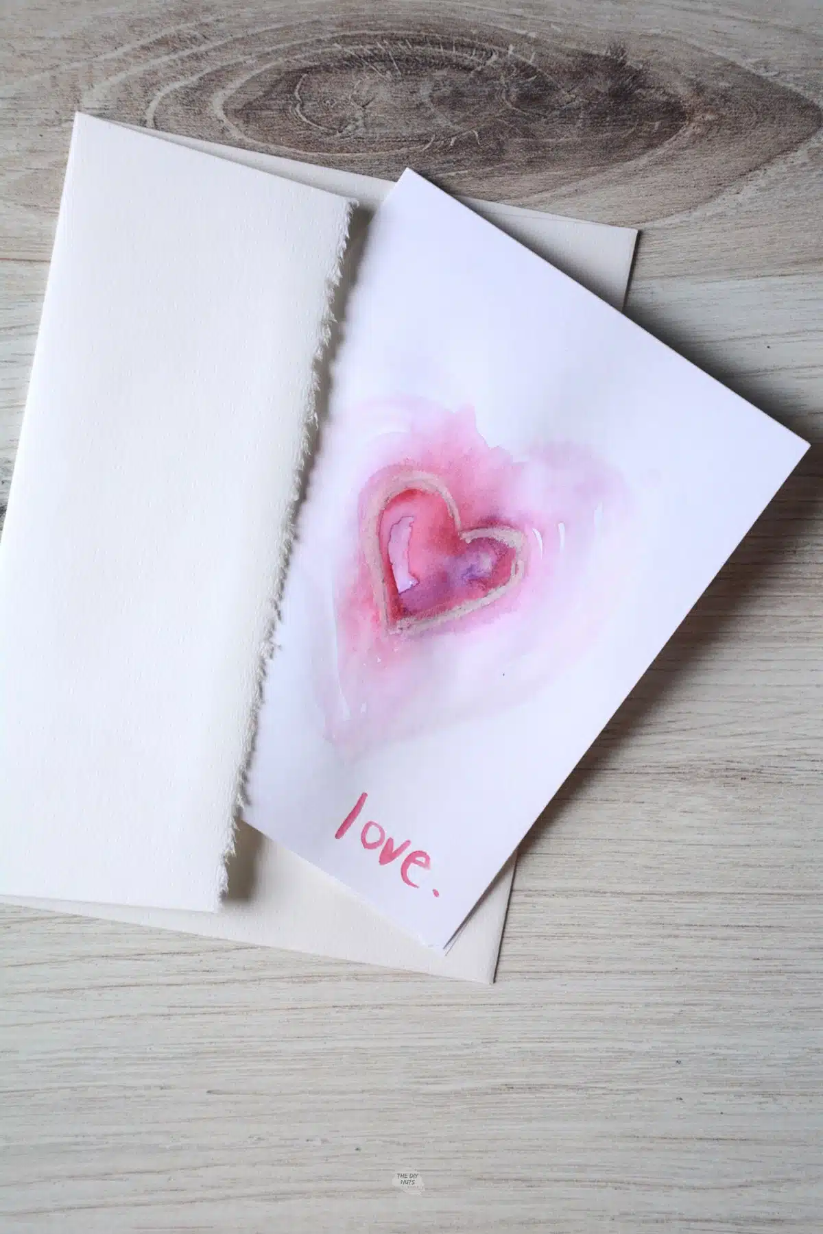 watercolor heart card on white paper with heart in center in white envelope.
