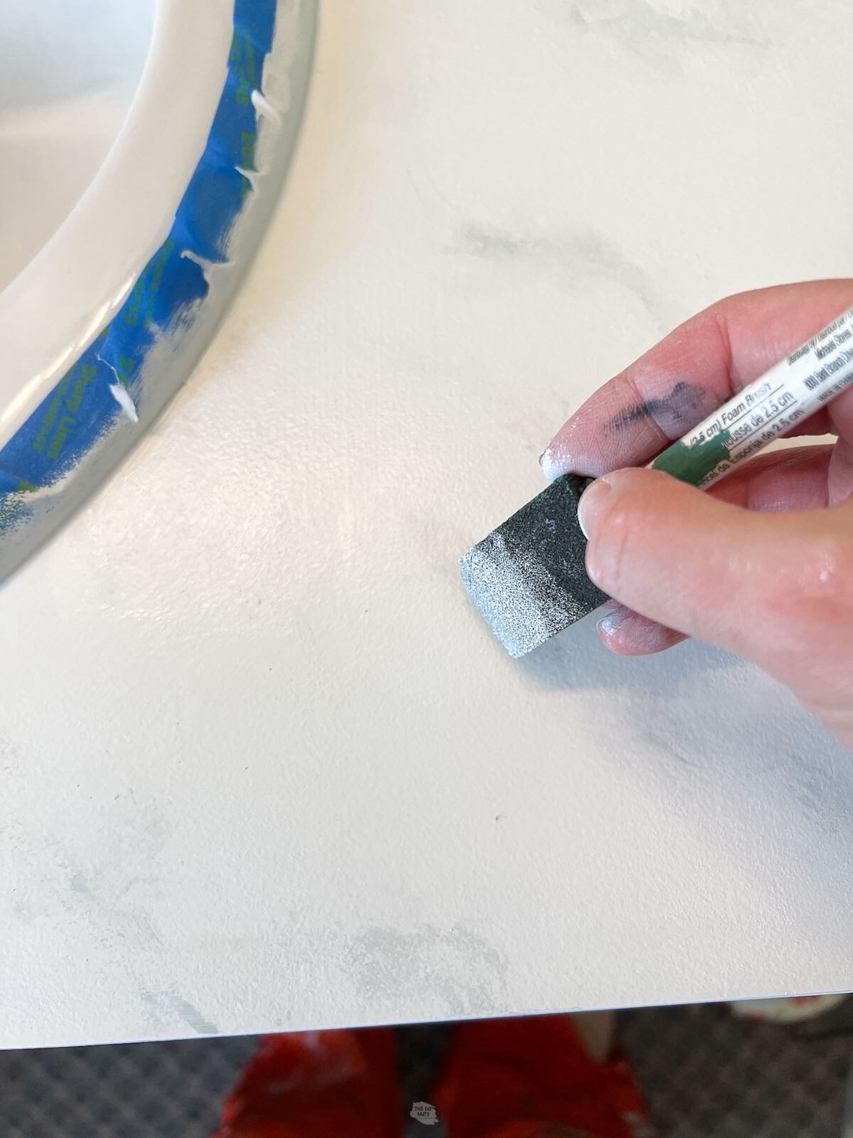 hand holding small foam brush adding white paint on countertops.