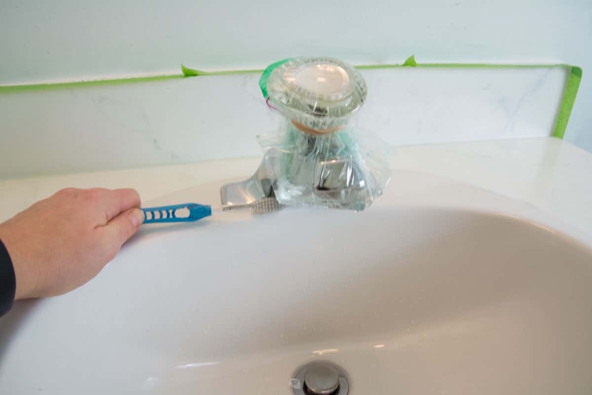 hand holding toothbrush cleaning with bag of liquid rubber band on end of spout.