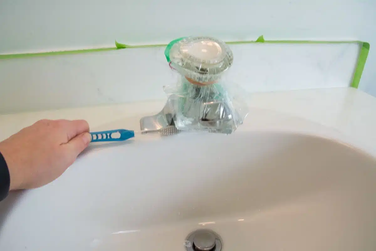 hand holding toothbrush cleaning with bag of liquid rubber band on end of spout.