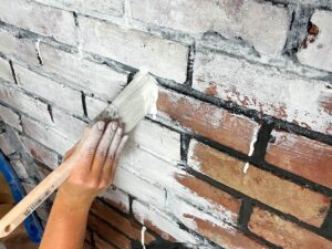 hand holding paint brush adding white to brick.