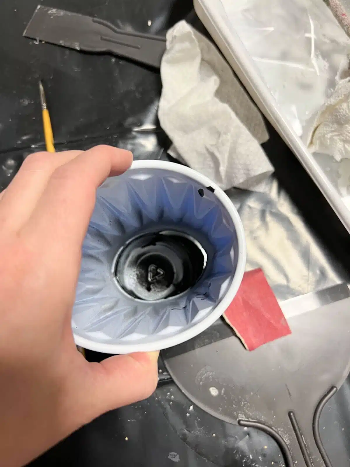 hand holding plastic cup with spray paint and hole in cup.
