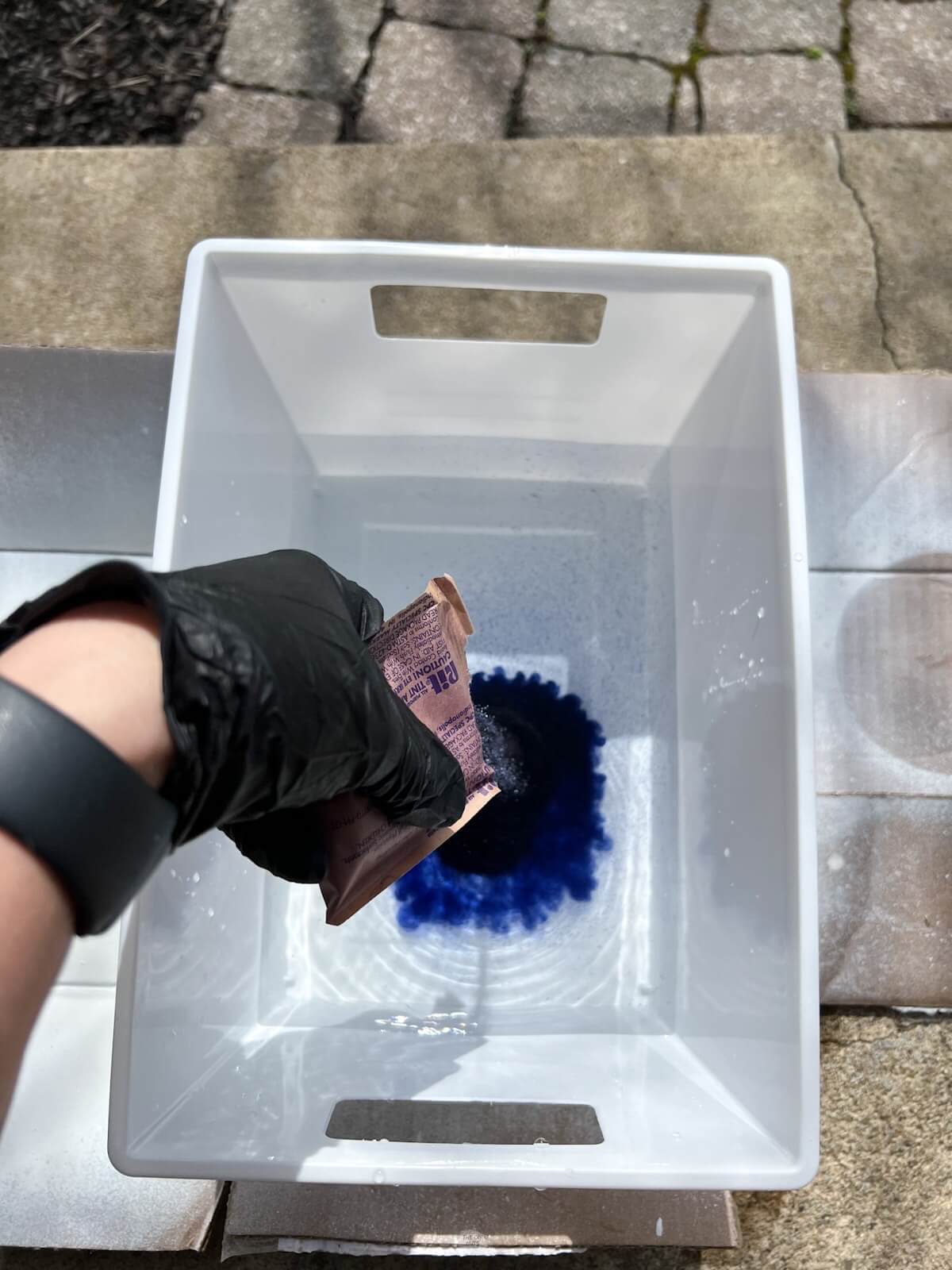 hand wearing glove pouring powder blue dye into water.
