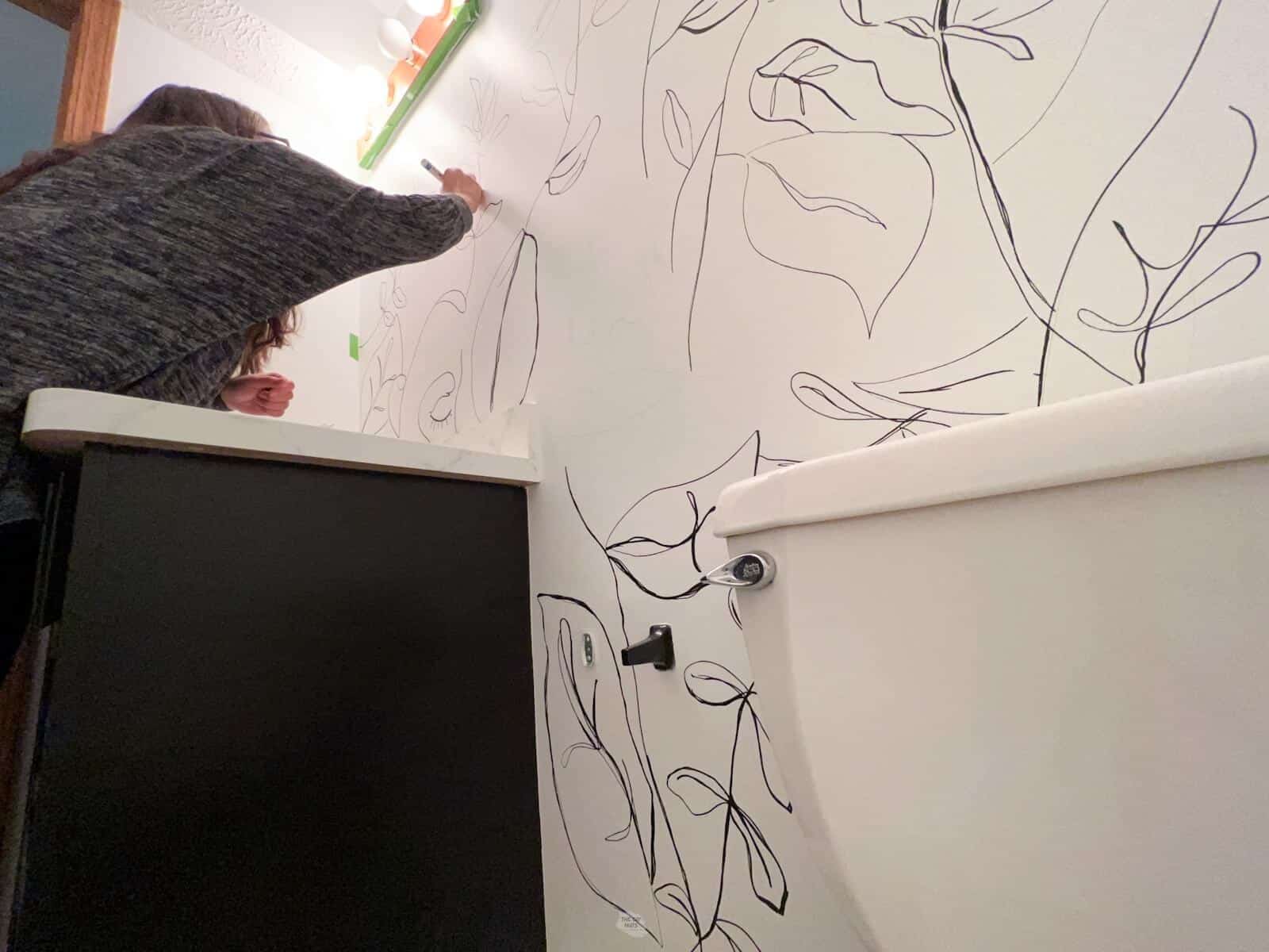 woman drawing floral organic design with paint marker on white walls in bathroom.