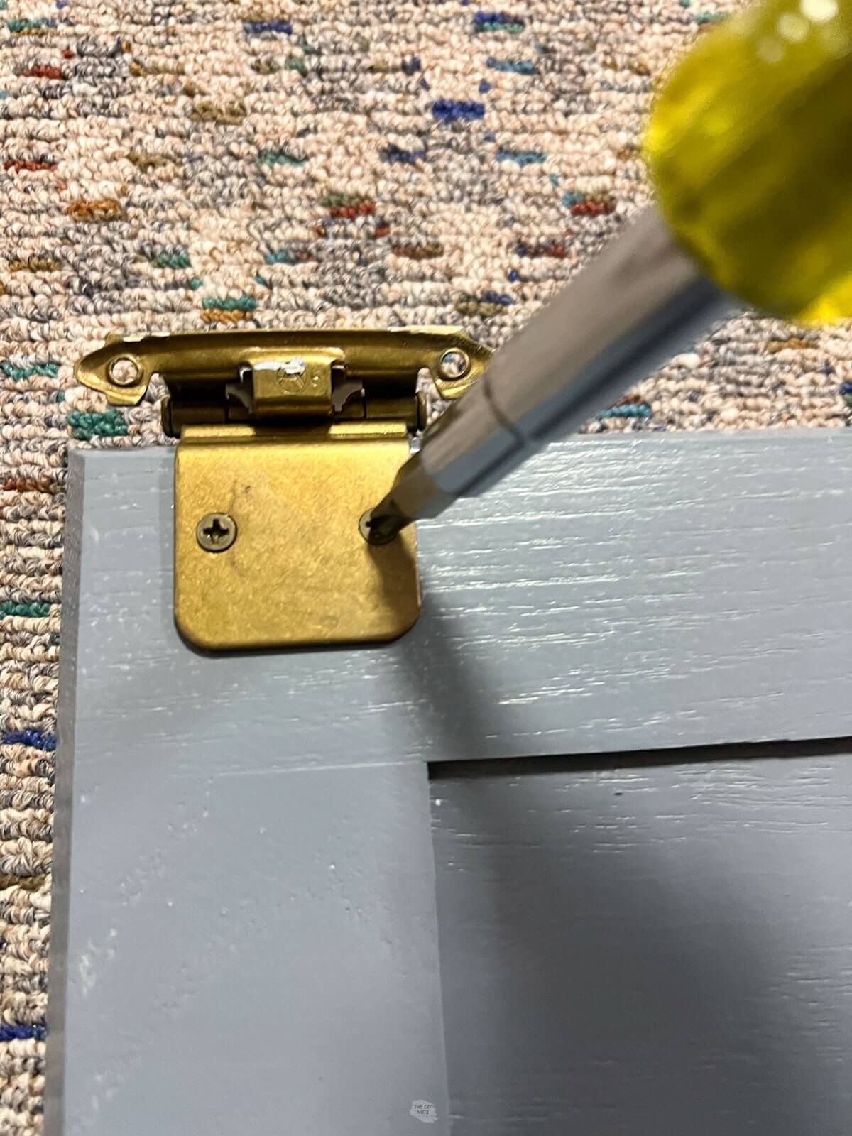 screwdriver on cabinet hinge on painted gray door.