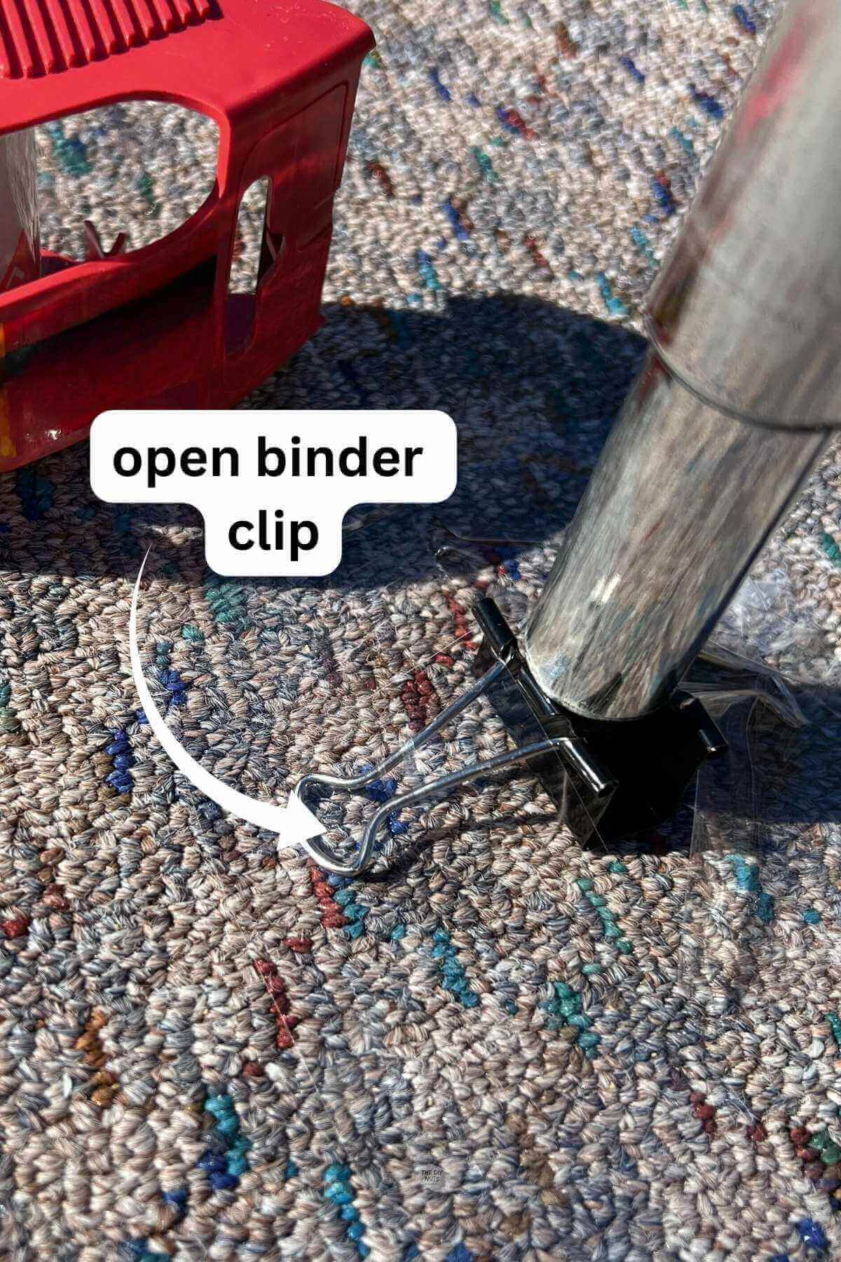 binder clip open and tape to carpet with silver toilet paper roll being held by binder clip.