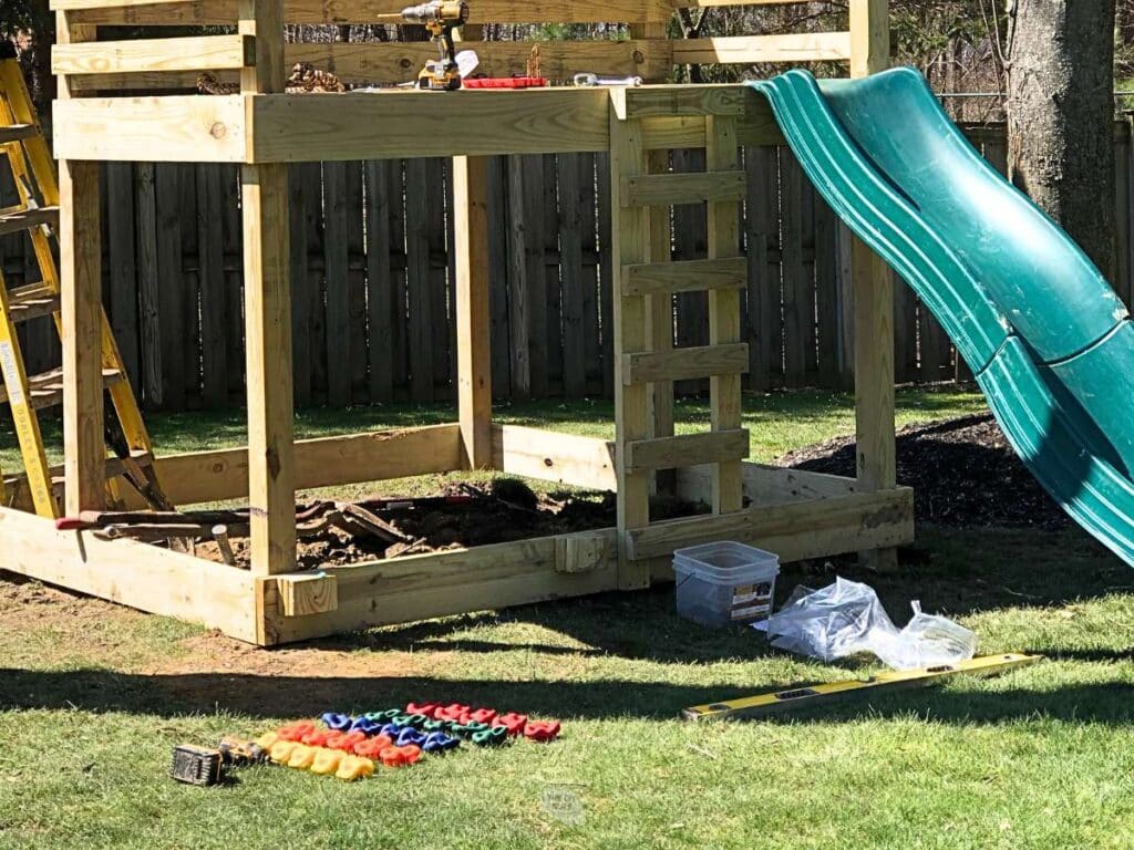 diy playset with rock holds on the ground and green plastic slide.