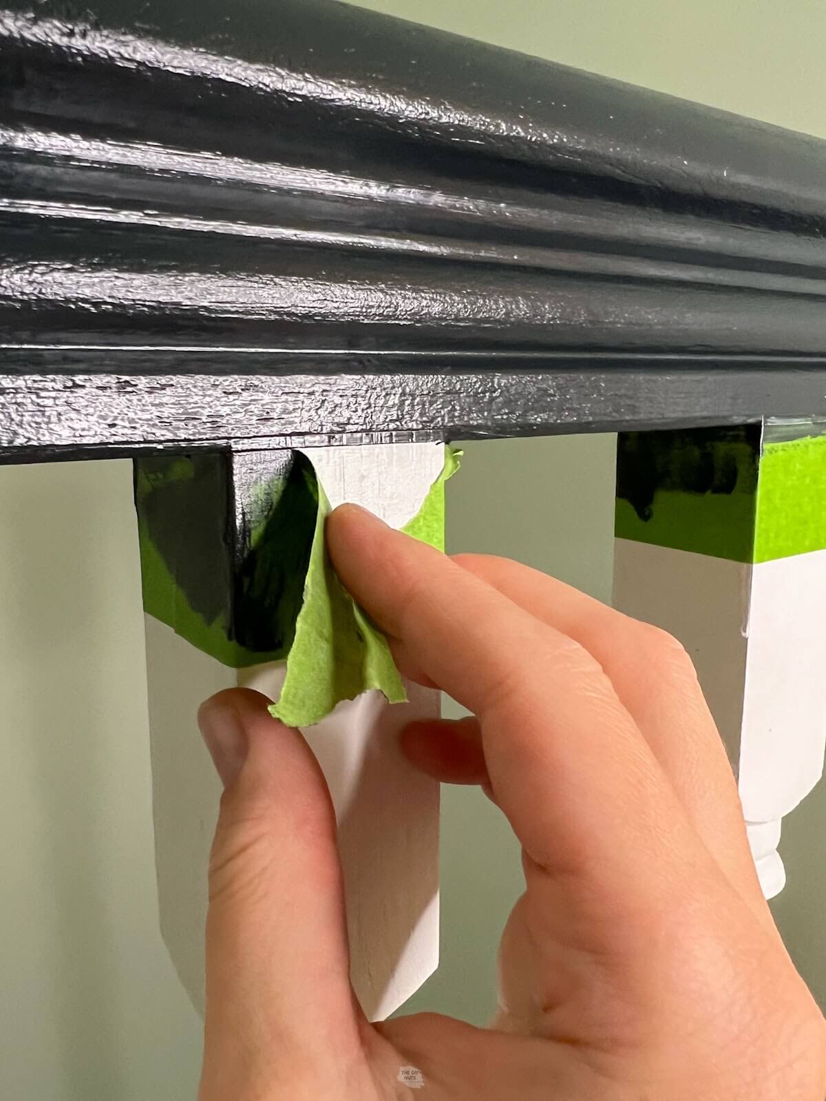 hand pulling green painter's tape off of black and white painted railing.