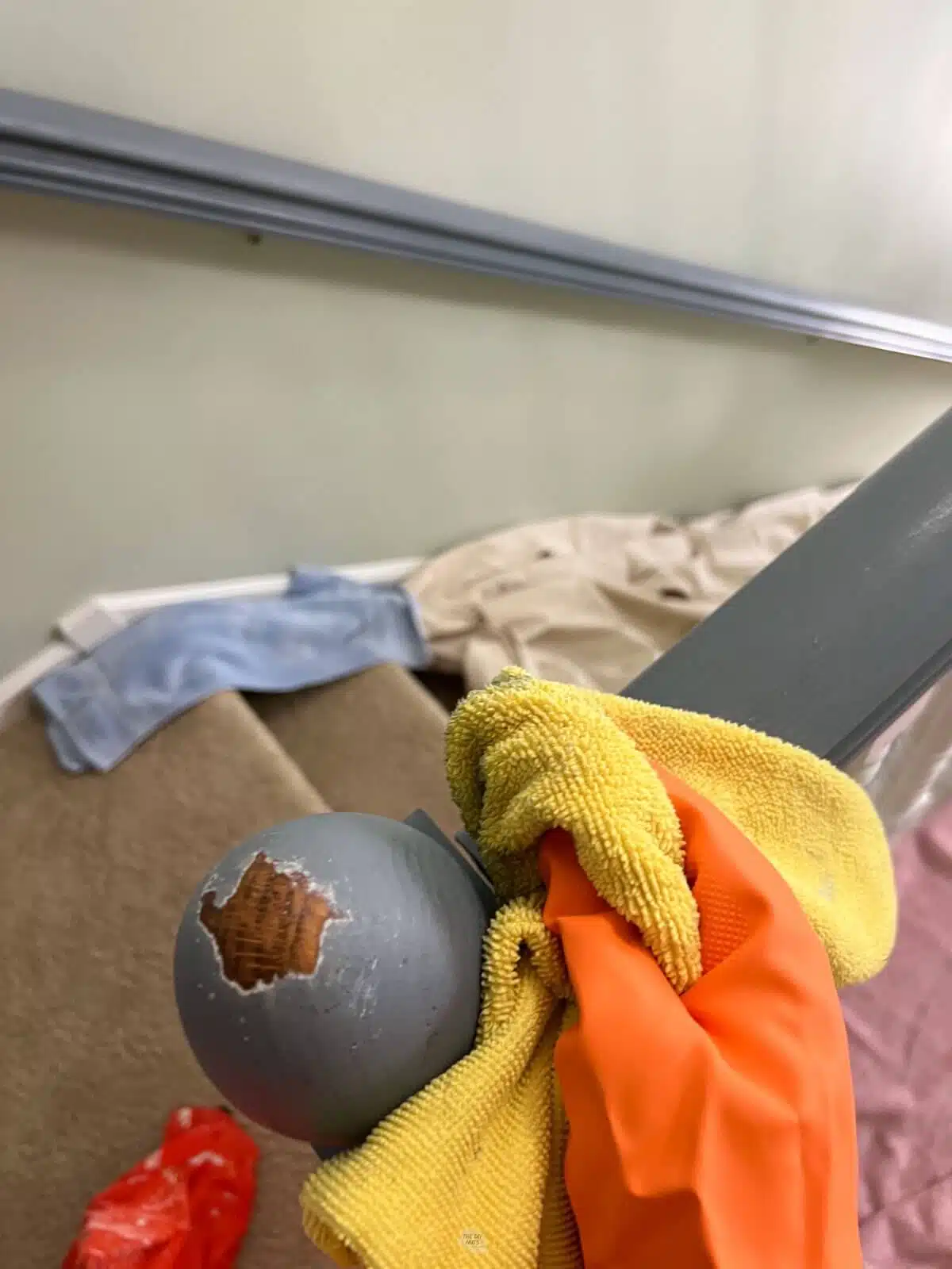 hand wearing orange rubber glove wiping down painted stair railing with yellow rag.