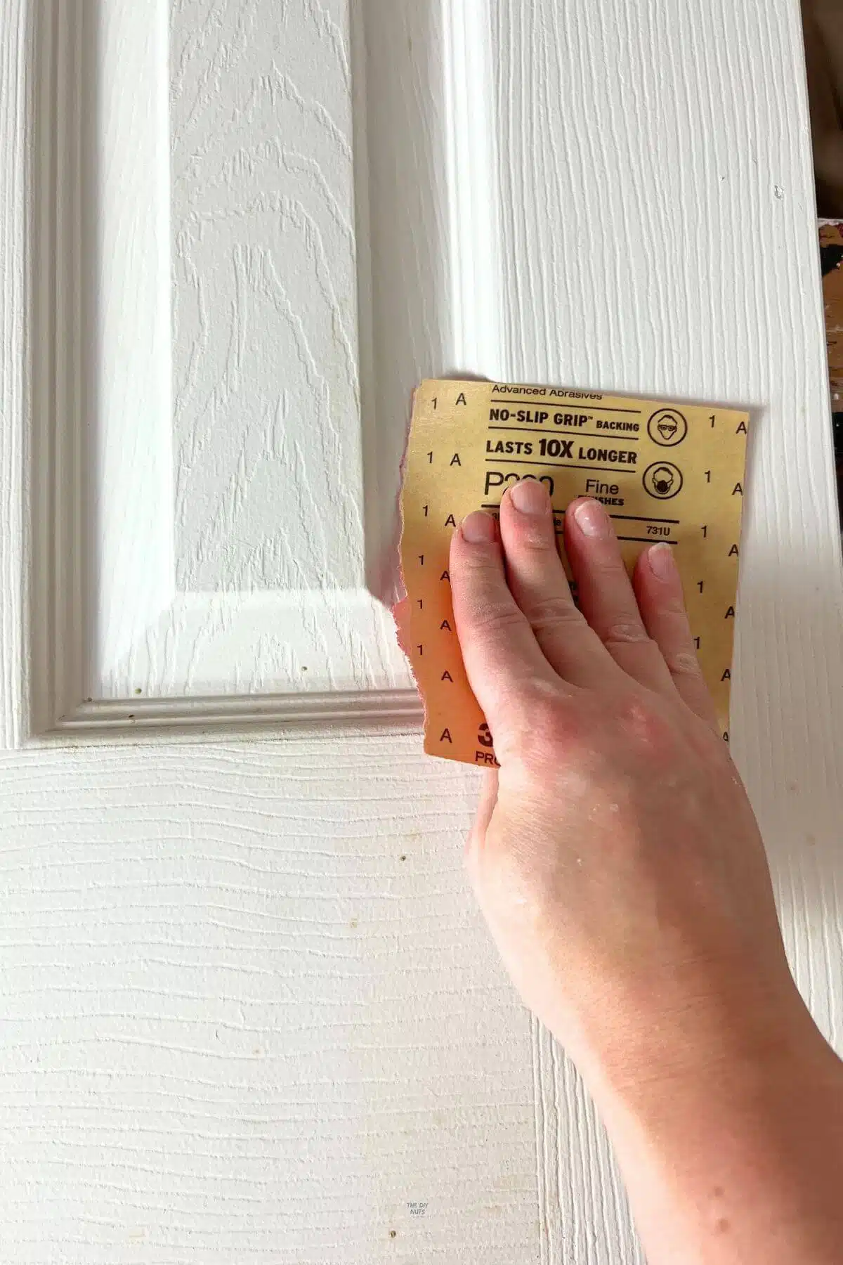 hand holding 220 sandpaper on white surface of interior door.