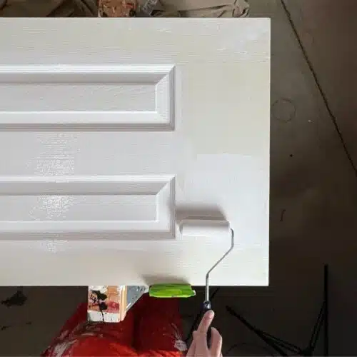 hand holding small roller adding white paint interior door on sawhorses.