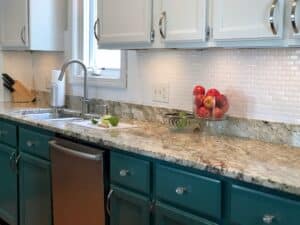 white painted backsplash tile in kitchen with granite counters and green and white cabinets.