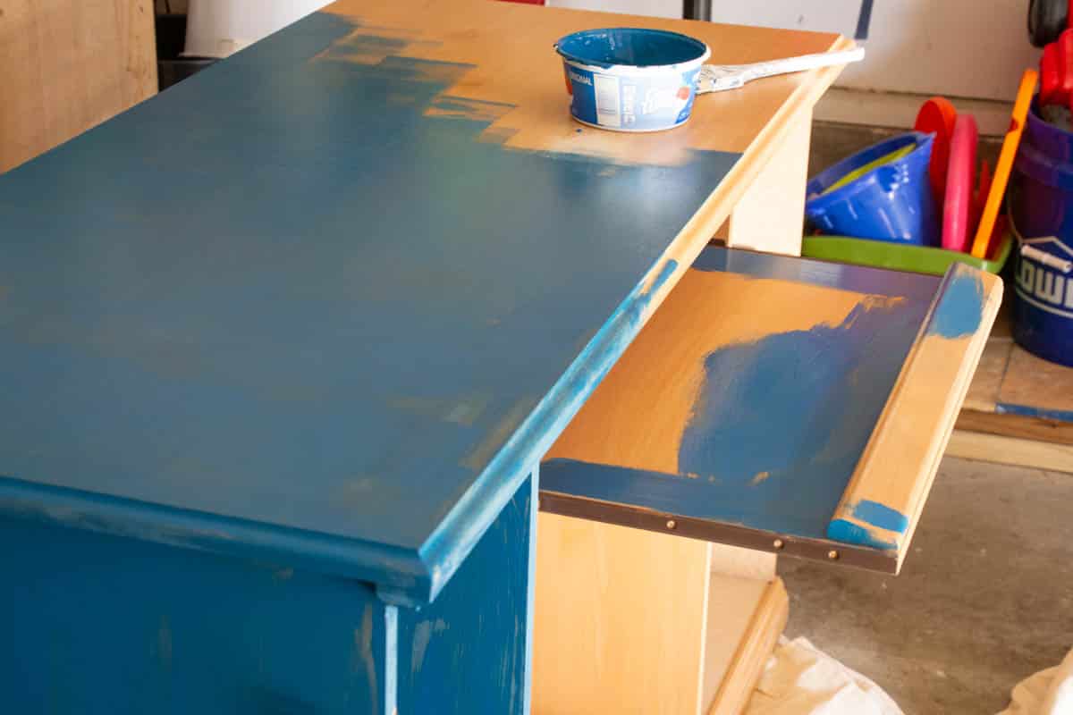 tan desk with some blue paint on it in a garage.