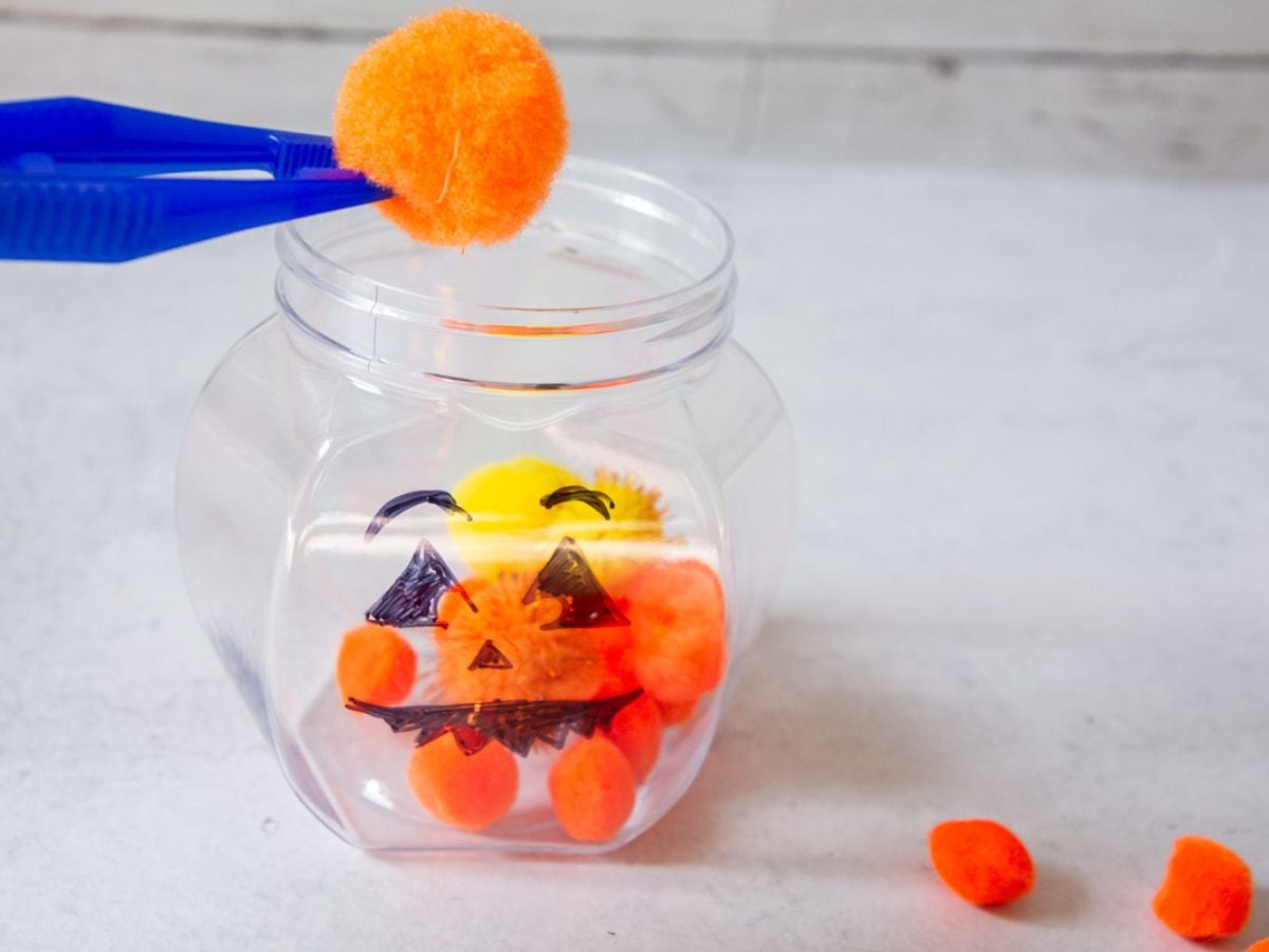 orange poof ball going into plastic cup.