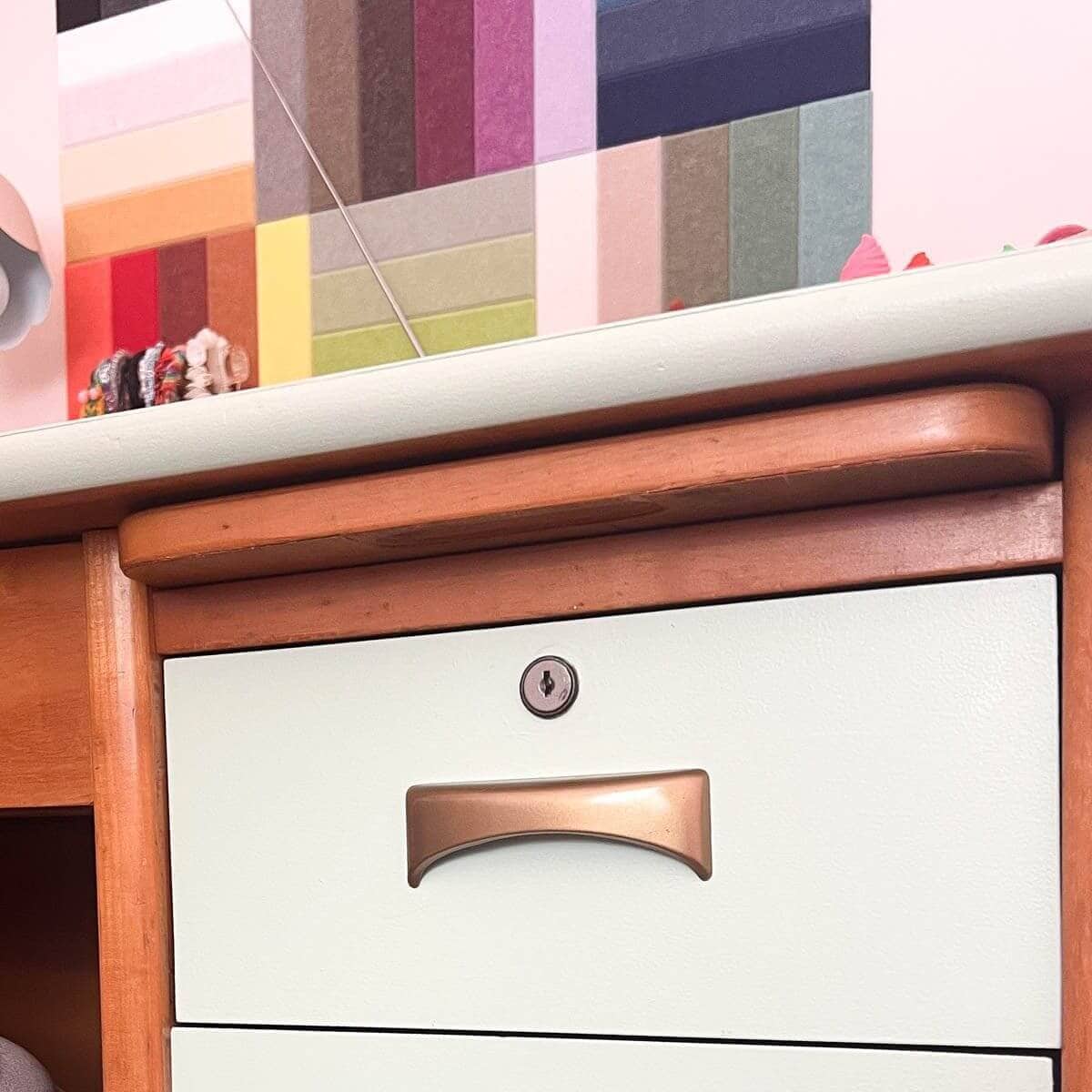 gold hardware handle on light green and wood desk.